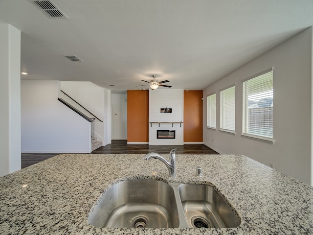 kitchen featuring light stone counters, ceiling fan, sink, a fireplace, and dark hardwood / wood-style floors