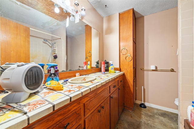 bathroom with concrete flooring, vanity, a textured ceiling, tiled shower, and toilet