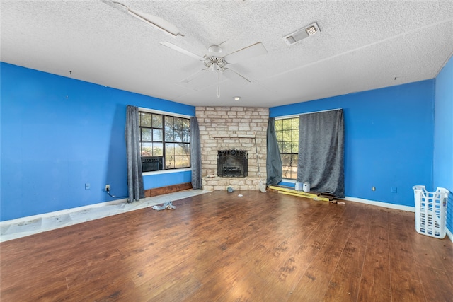 unfurnished living room with hardwood / wood-style floors, a textured ceiling, a stone fireplace, and ceiling fan