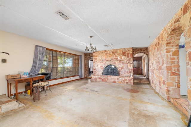 unfurnished living room featuring concrete flooring, a stone fireplace, a chandelier, and a textured ceiling