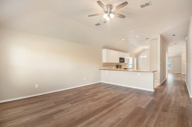 unfurnished living room featuring ceiling fan with notable chandelier, dark wood-type flooring, and vaulted ceiling