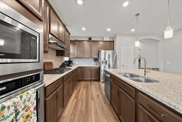 kitchen featuring light stone countertops, sink, hanging light fixtures, light hardwood / wood-style floors, and appliances with stainless steel finishes