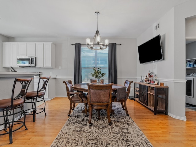 dining area with a chandelier, washer / clothes dryer, and light hardwood / wood-style flooring