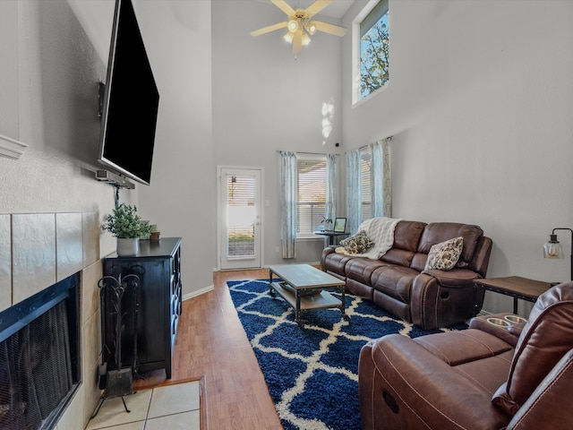 living room with ceiling fan, a towering ceiling, a healthy amount of sunlight, and light hardwood / wood-style floors