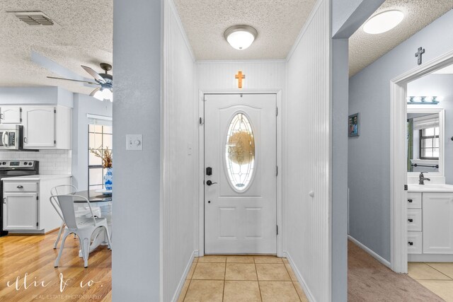 foyer featuring light tile patterned floors, a textured ceiling, a wealth of natural light, and ceiling fan