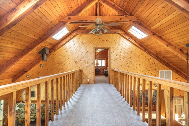 corridor with carpet, wood walls, vaulted ceiling with skylight, and wooden ceiling