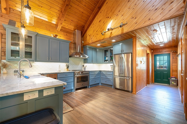 kitchen featuring pendant lighting, high quality appliances, wall chimney range hood, and wooden walls