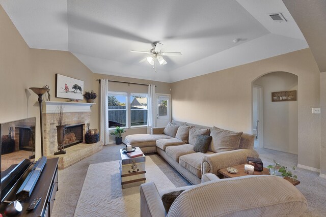 living room with lofted ceiling, ceiling fan, a tray ceiling, light carpet, and a brick fireplace