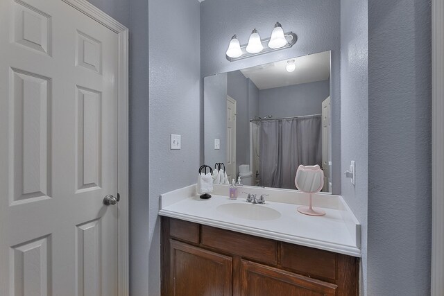 bathroom featuring vanity, walk in shower, and toilet