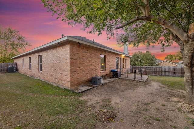 property exterior at dusk with a yard, central AC unit, and a patio area