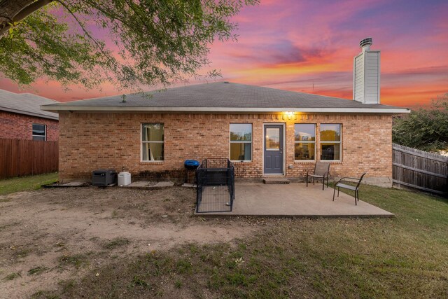 back house at dusk featuring a patio area and a lawn