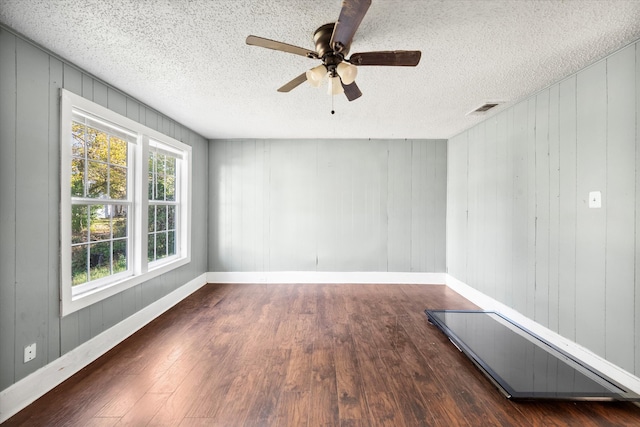 empty room featuring dark hardwood / wood-style flooring, a textured ceiling, and wooden walls