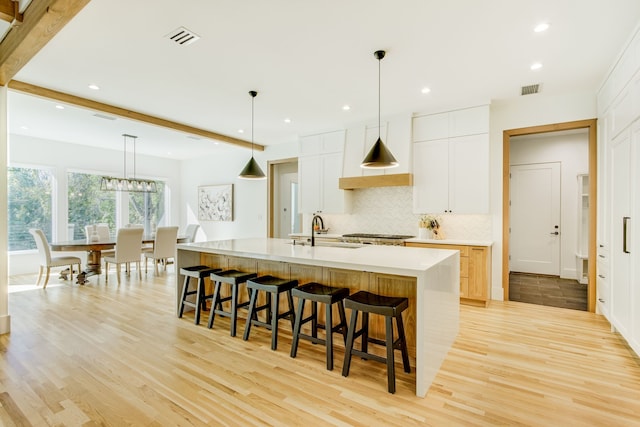 kitchen featuring a spacious island, sink, decorative light fixtures, light hardwood / wood-style floors, and white cabinetry