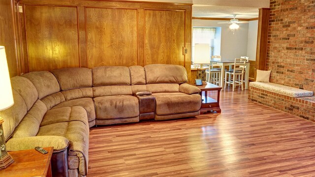 living room featuring ceiling fan, light hardwood / wood-style flooring, and brick wall