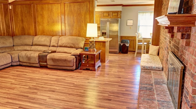 living room featuring crown molding, a fireplace, light hardwood / wood-style floors, and brick wall