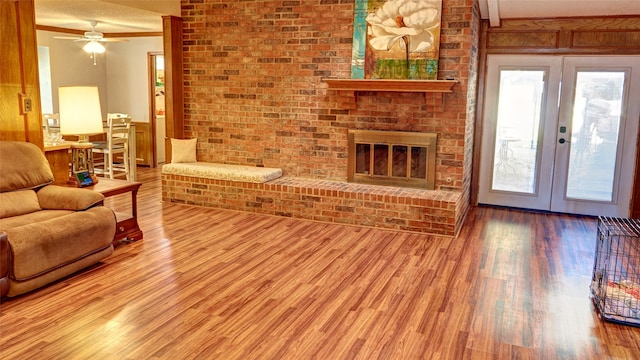 living room featuring french doors, a brick fireplace, hardwood / wood-style flooring, ceiling fan, and a textured ceiling