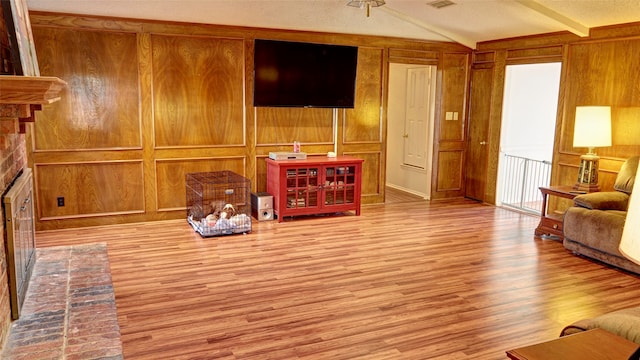 living room with a brick fireplace, lofted ceiling with beams, wood walls, light hardwood / wood-style floors, and a textured ceiling