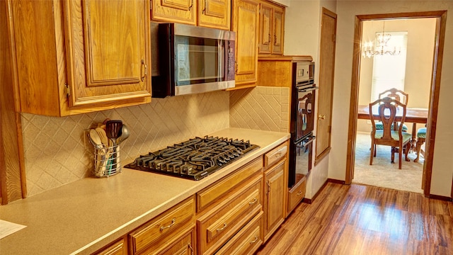 kitchen with wood-type flooring, stainless steel appliances, an inviting chandelier, and tasteful backsplash