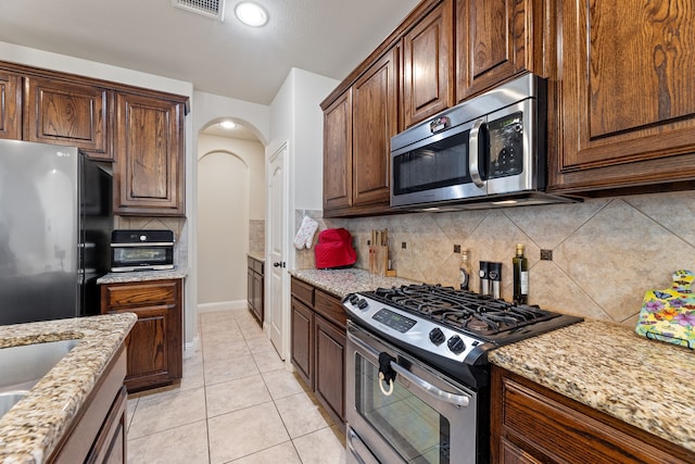 kitchen featuring backsplash, light stone countertops, stainless steel appliances, and light tile patterned floors