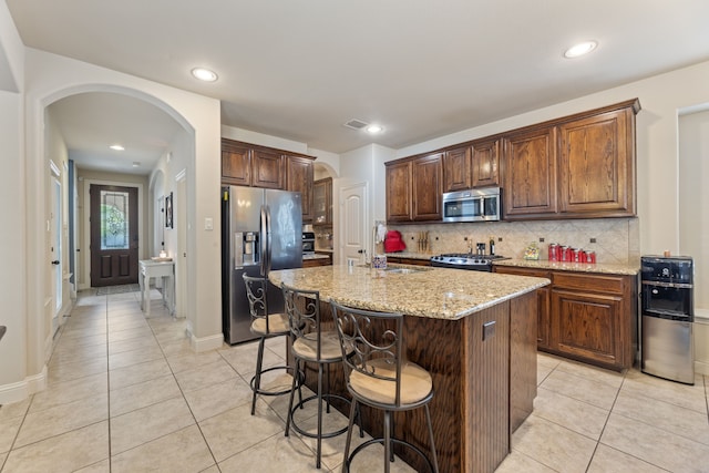 kitchen with a center island with sink, light stone counters, light tile patterned floors, and appliances with stainless steel finishes