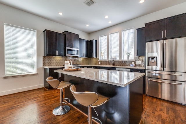 kitchen with a breakfast bar, light stone counters, appliances with stainless steel finishes, dark hardwood / wood-style flooring, and a kitchen island