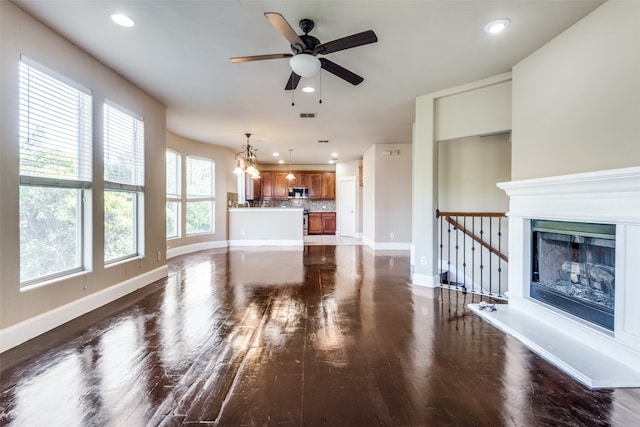 unfurnished living room with ceiling fan with notable chandelier and dark hardwood / wood-style flooring