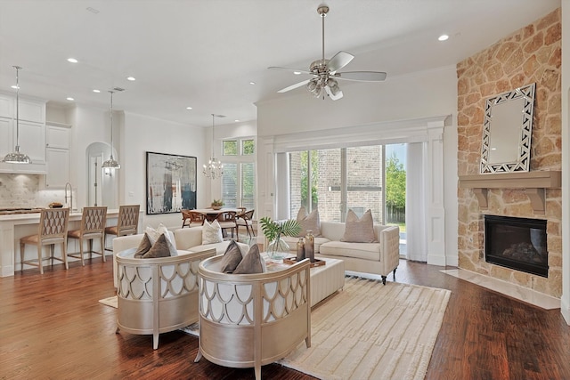 living room with hardwood / wood-style floors, ceiling fan with notable chandelier, a stone fireplace, sink, and crown molding