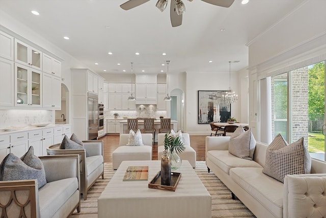 living room featuring crown molding, sink, light hardwood / wood-style floors, and ceiling fan with notable chandelier