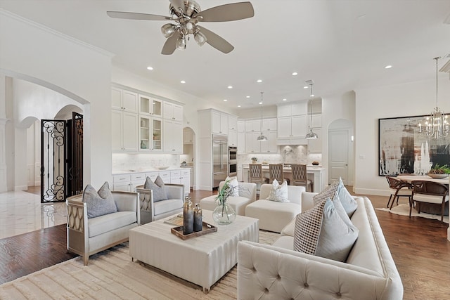 living room with ceiling fan with notable chandelier, crown molding, and light hardwood / wood-style flooring