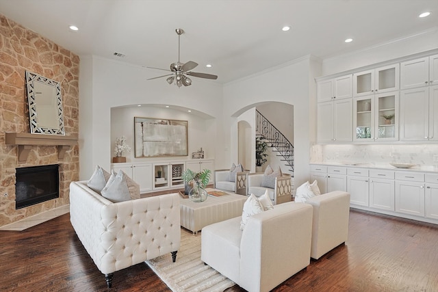 living room with dark hardwood / wood-style flooring, a stone fireplace, ceiling fan, and crown molding