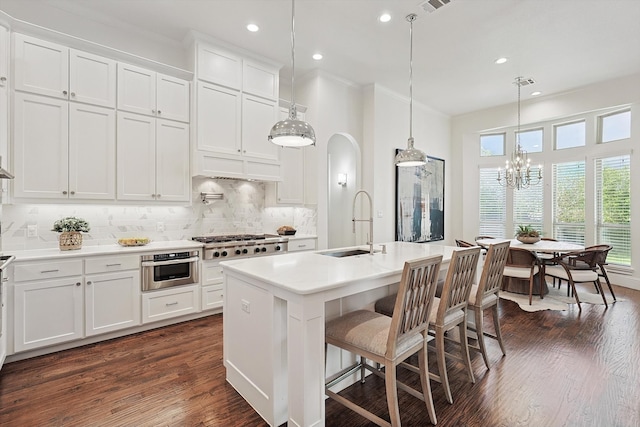 kitchen with white cabinetry, dark hardwood / wood-style flooring, pendant lighting, a kitchen island with sink, and appliances with stainless steel finishes