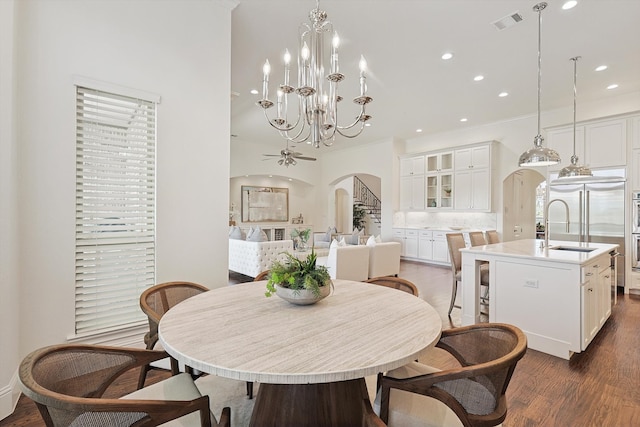 dining area with ceiling fan with notable chandelier, sink, and dark wood-type flooring