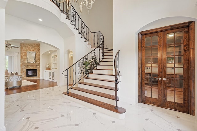 staircase featuring a fireplace, french doors, a towering ceiling, and ceiling fan