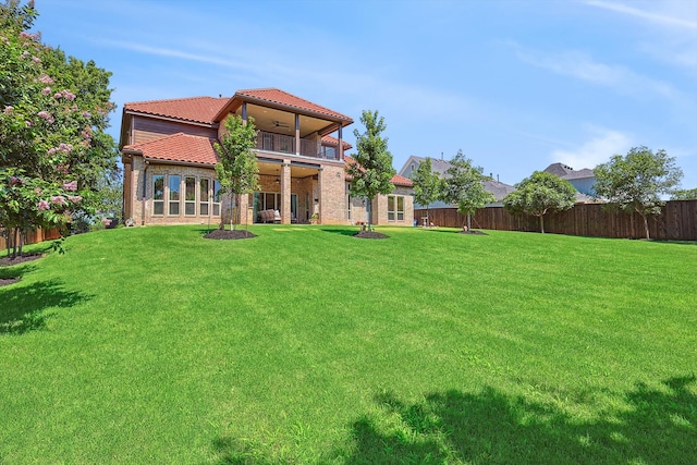 rear view of house with a balcony, ceiling fan, and a lawn