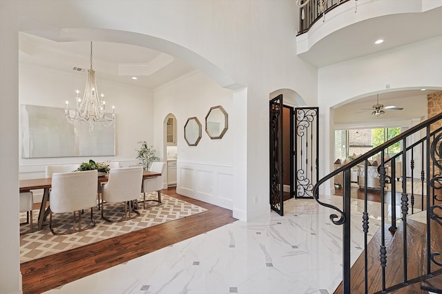 foyer entrance featuring hardwood / wood-style floors, a high ceiling, ceiling fan with notable chandelier, and ornamental molding