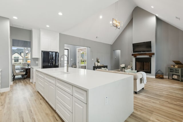 kitchen with black refrigerator, a kitchen island with sink, sink, light hardwood / wood-style flooring, and white cabinets