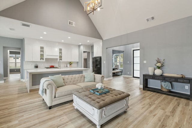 living room featuring a notable chandelier, plenty of natural light, light hardwood / wood-style floors, and high vaulted ceiling