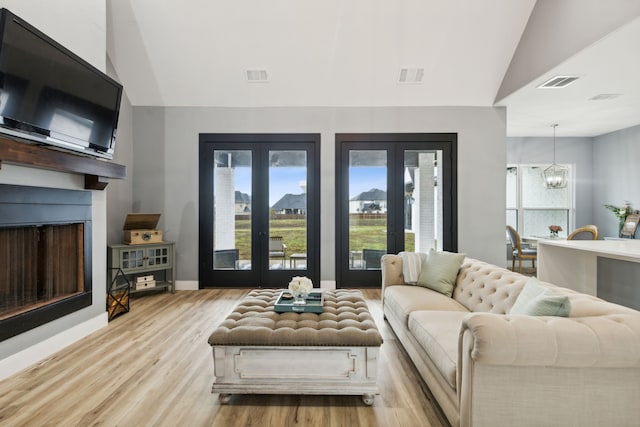 living room with french doors, light hardwood / wood-style floors, vaulted ceiling, and an inviting chandelier