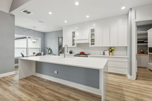 kitchen featuring light wood-type flooring, tasteful backsplash, sink, a center island with sink, and white cabinetry