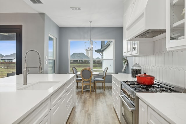 kitchen featuring white cabinets, stainless steel stove, hanging light fixtures, and custom exhaust hood