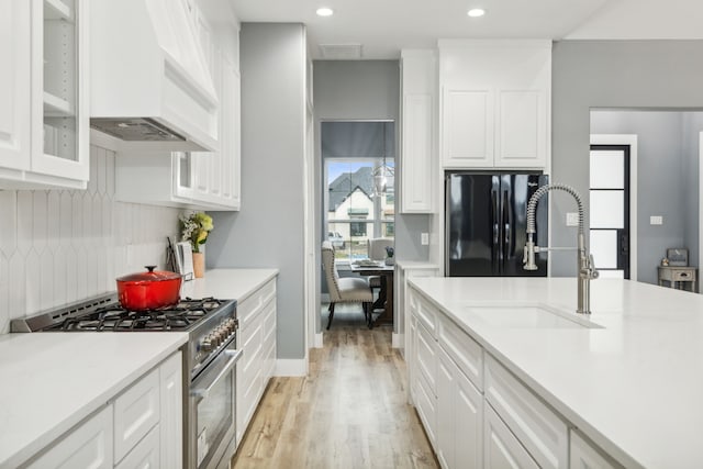 kitchen with white cabinetry, black fridge, stainless steel range, and sink