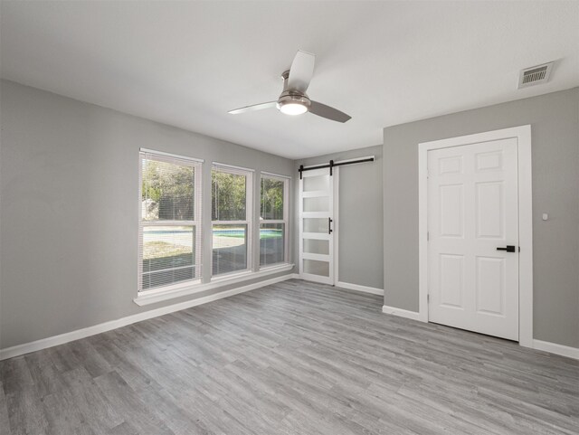 unfurnished bedroom featuring a barn door, ceiling fan, and light hardwood / wood-style flooring