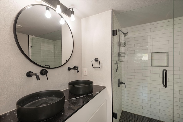 full bath with a textured wall, a stall shower, and a sink