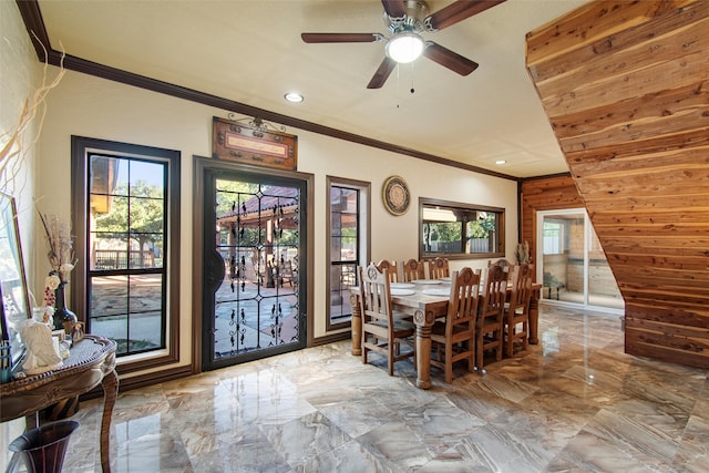 unfurnished dining area with wooden walls, ceiling fan, crown molding, and a wealth of natural light