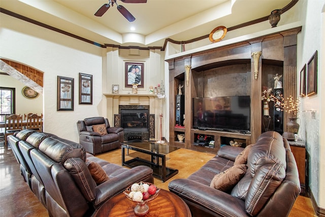 living room featuring a fireplace, a tray ceiling, ceiling fan, and crown molding