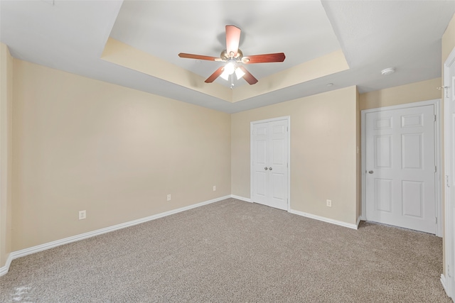 spare room with ceiling fan, a raised ceiling, and light colored carpet