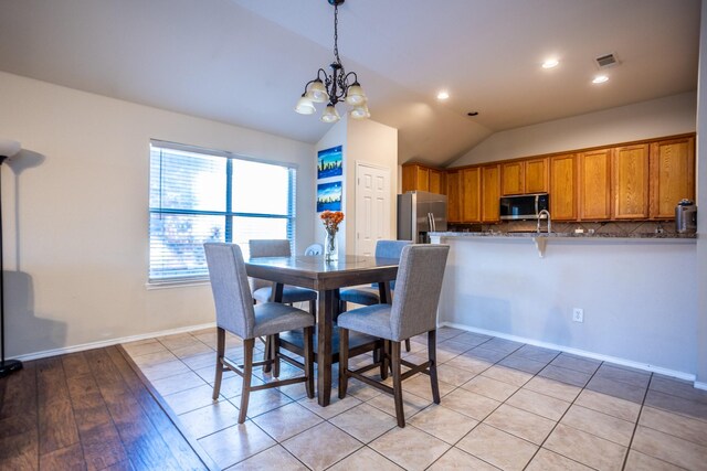 dining area with light hardwood / wood-style floors, an inviting chandelier, and vaulted ceiling