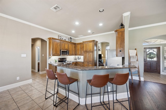 kitchen featuring stainless steel appliances, a kitchen bar, ornamental molding, and kitchen peninsula