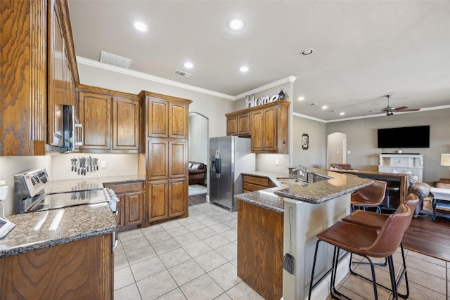 kitchen featuring a kitchen breakfast bar, kitchen peninsula, range, dark stone counters, and stainless steel fridge with ice dispenser