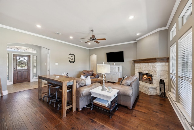 living room featuring a stone fireplace, ornamental molding, ceiling fan, and dark hardwood / wood-style floors